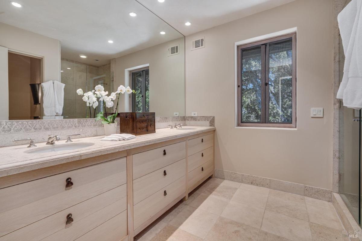 Bathroom with dual sinks, a large mirror, and a glass shower enclosure.
