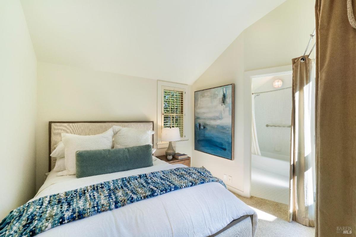 Bedroom with a bed, corner windows, and white shutters.