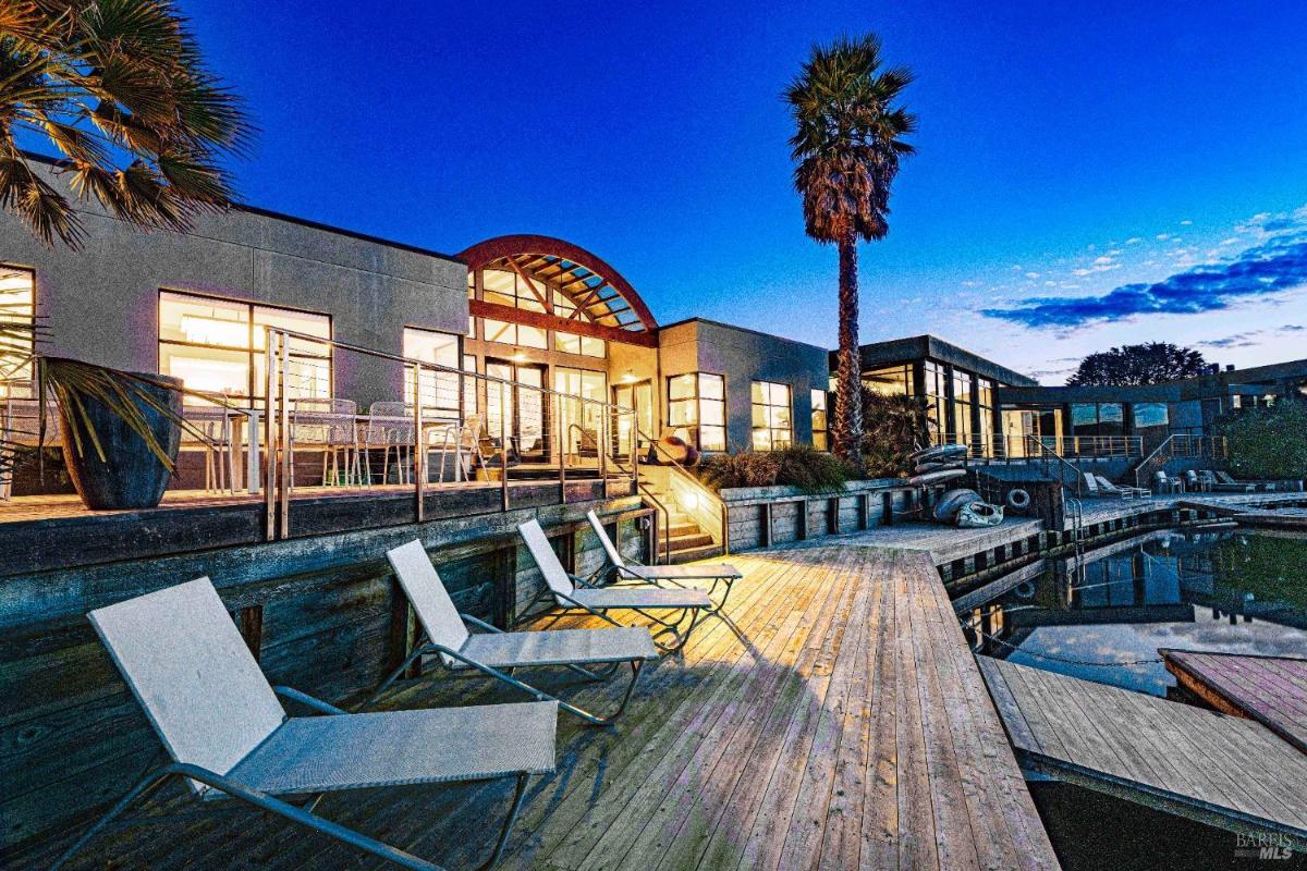 A dock with lounge chairs and a modern house at dusk. 