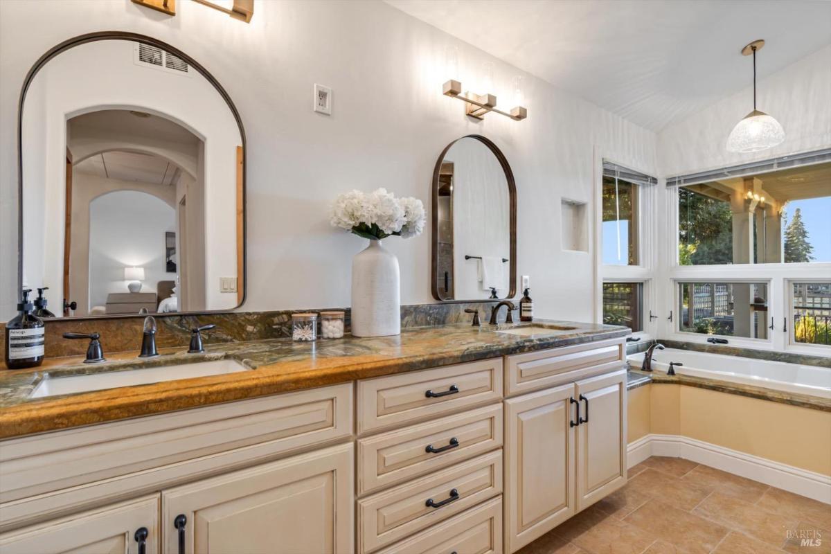 Bathroom with dual sinks, a bathtub, and large windows.