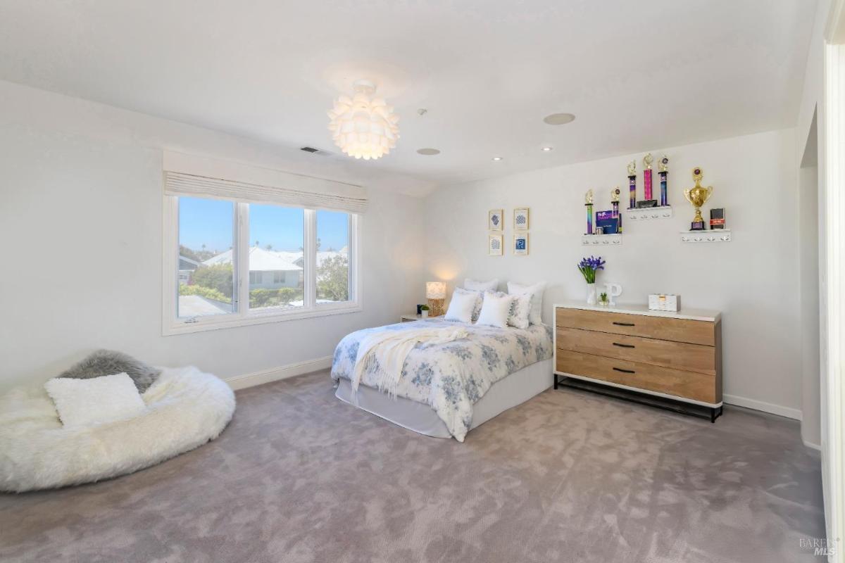 Bedroom with a bed, dresser, wall decor, and large windows facing the neighborhood.