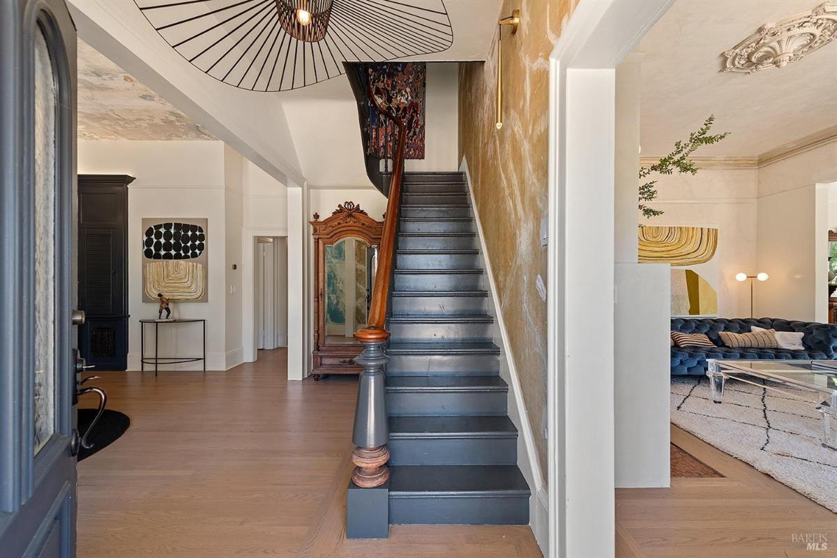 Foyer with dark-painted staircase, decorative ceiling, and eclectic furnishings.