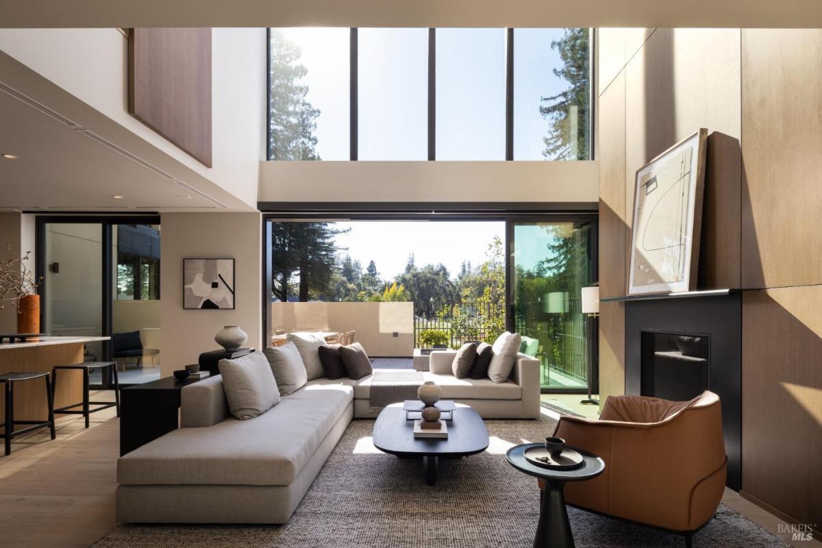 A spacious living room with large windows, a fireplace, and sliding doors leading to an outdoor patio.