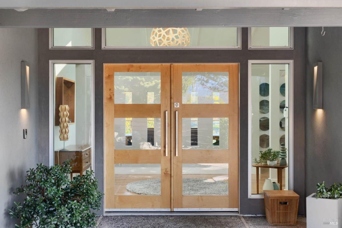A close-up of a modern wooden double-door entry with side windows and potted plants.