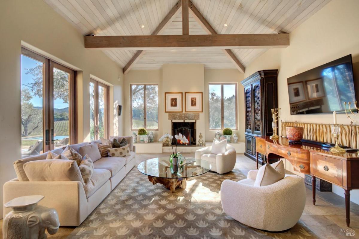 Living room with a vaulted ceiling, fireplace, large windows, and seating area.