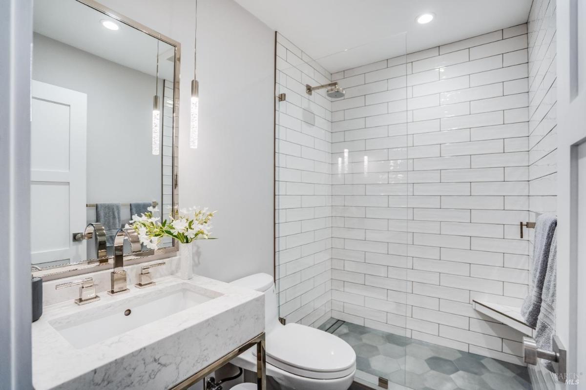 A bathroom with a glass shower, marble sink, and hexagonal floor tiles.
