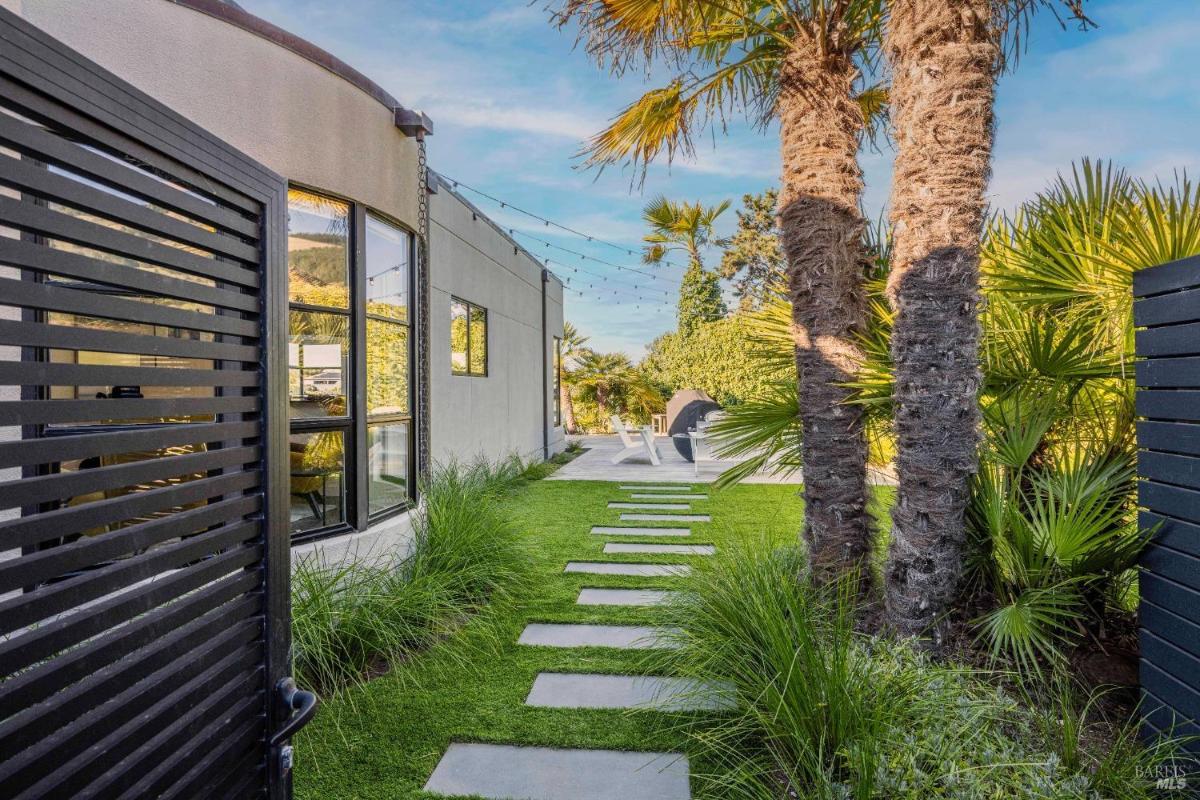 A pathway with stepping stones leads to a modern building surrounded by palm trees.