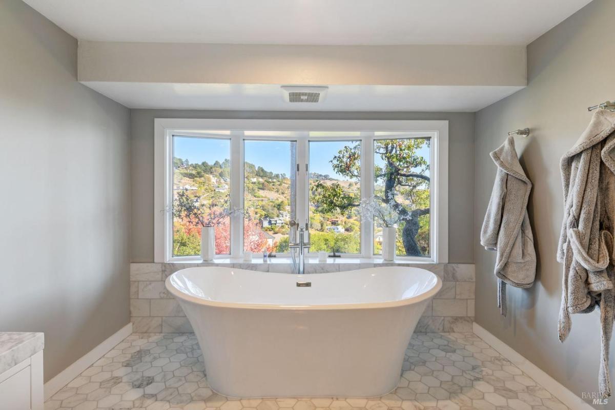 A bathroom featuring a freestanding bathtub, large windows with a scenic view, and a cozy atmosphere with soft colors.
