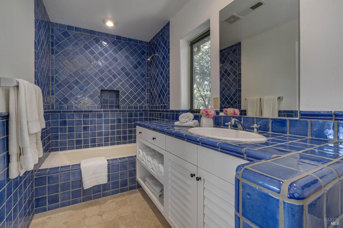 Bathroom with blue tiled walls, a combined tub and shower, and a single vanity.