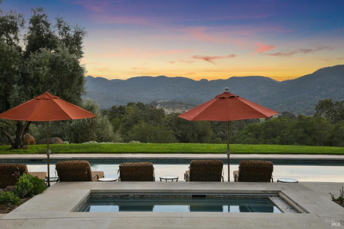 A pool with umbrellas and chairs facing a sunset mountain view.