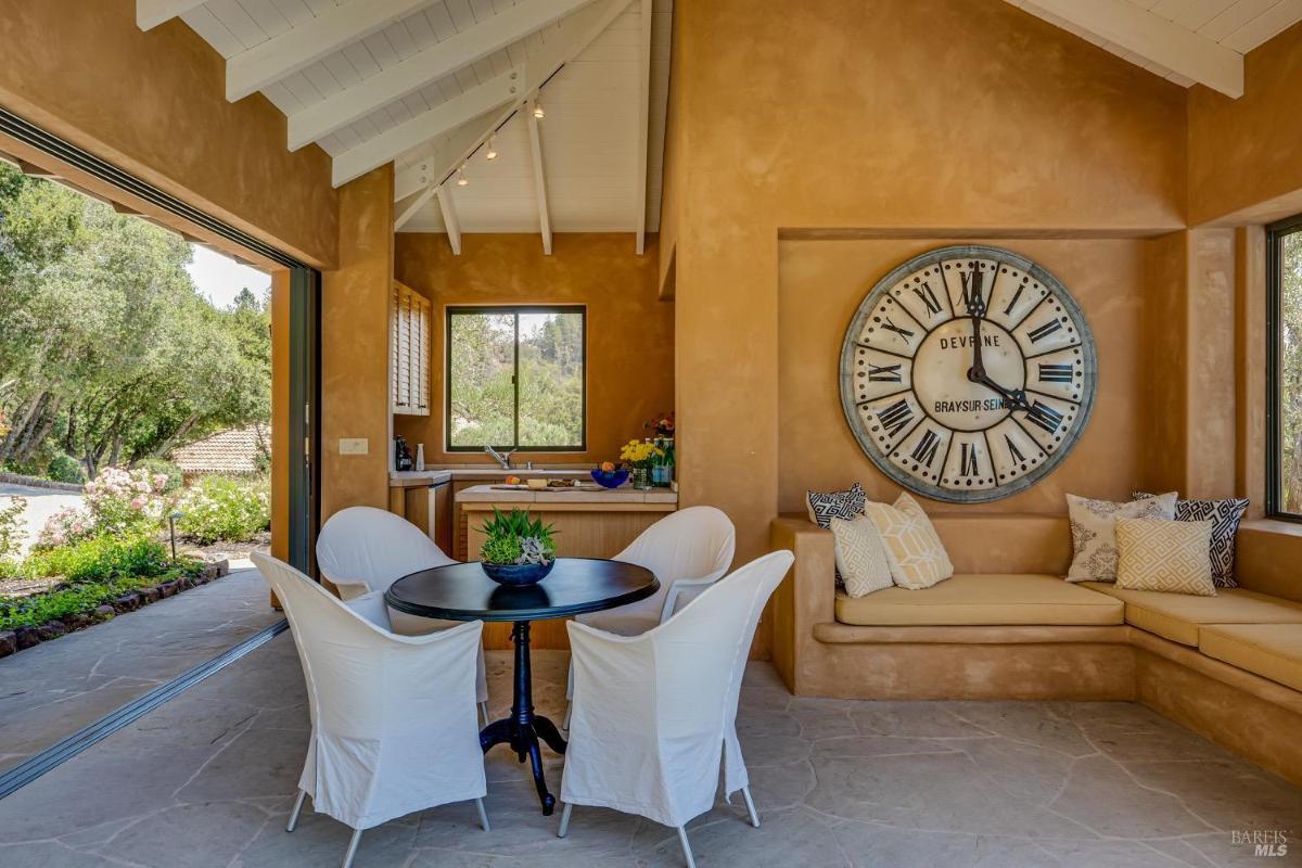 Outdoor seating area with a dining table, kitchenette, and large wall clock.