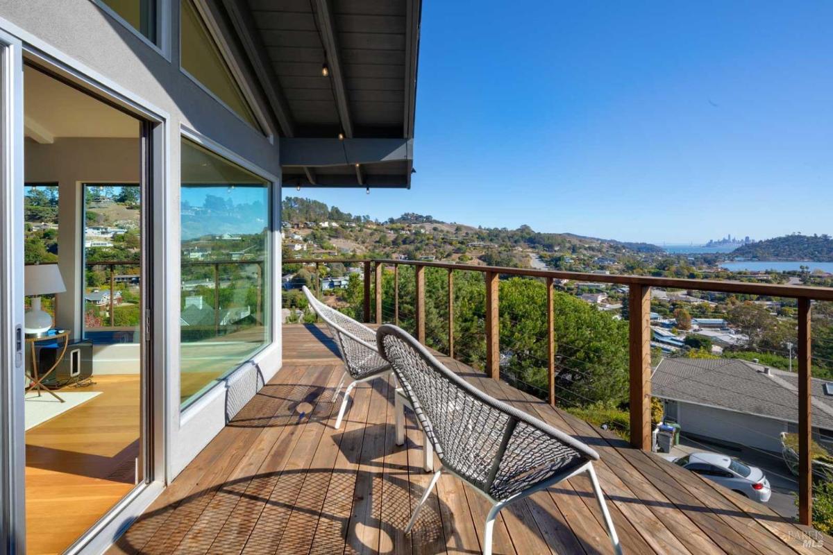 An outdoor deck with modern seating and a stunning view of the surrounding hills and water, showcasing a clear blue sky and a peaceful atmosphere.