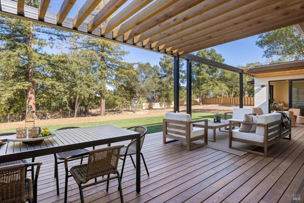 Outdoor deck with a dining table and chairs under a wooden pergola.