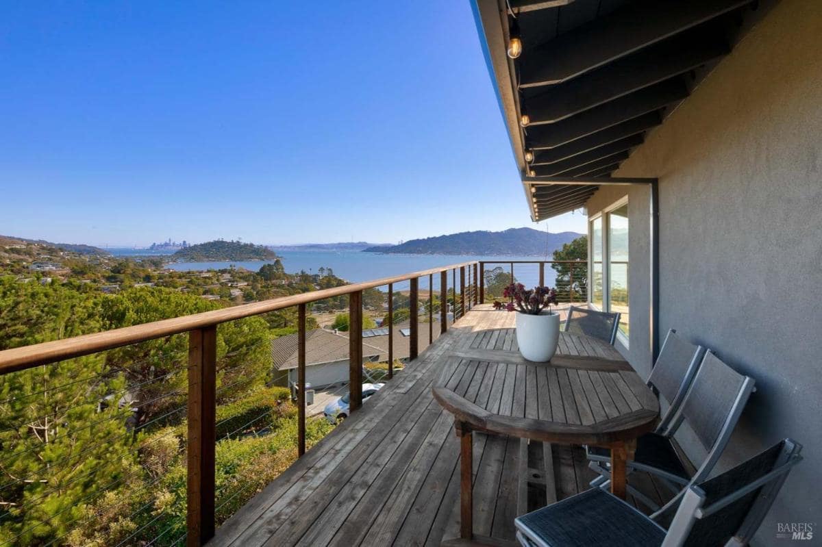 A wooden deck with a table and chairs overlooking water and hills.