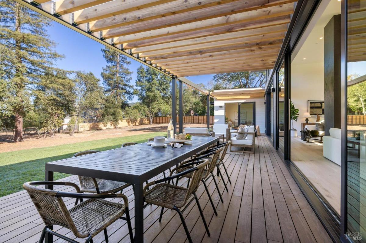 Wooden deck with outdoor seating and dining areas surrounded by greenery.