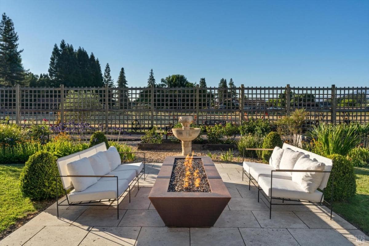 Outdoor seating area with a fire pit and a fountain in the background.