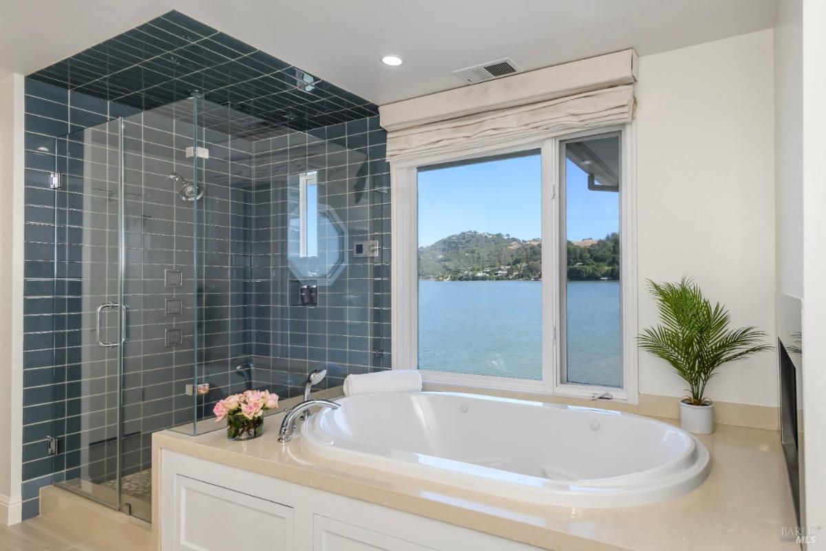 Bathroom with a bathtub, glass shower, and a water view.