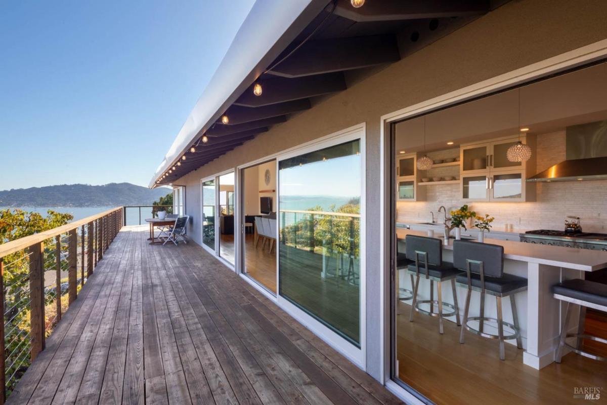 A wooden deck with a view of mountains and a kitchen area visible through large glass doors.