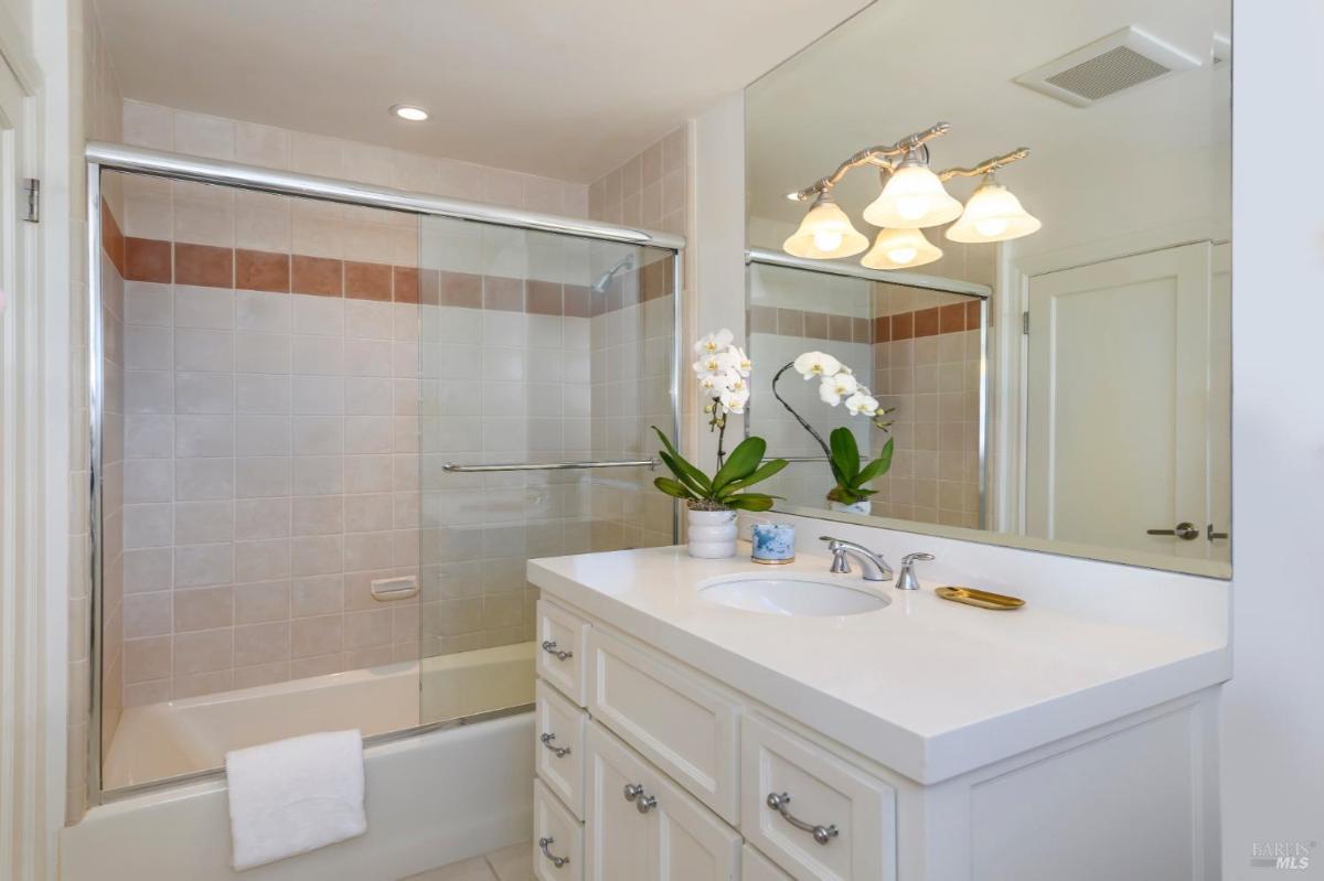 Bathroom with a vanity, tile accents, and a glass-enclosed tub.