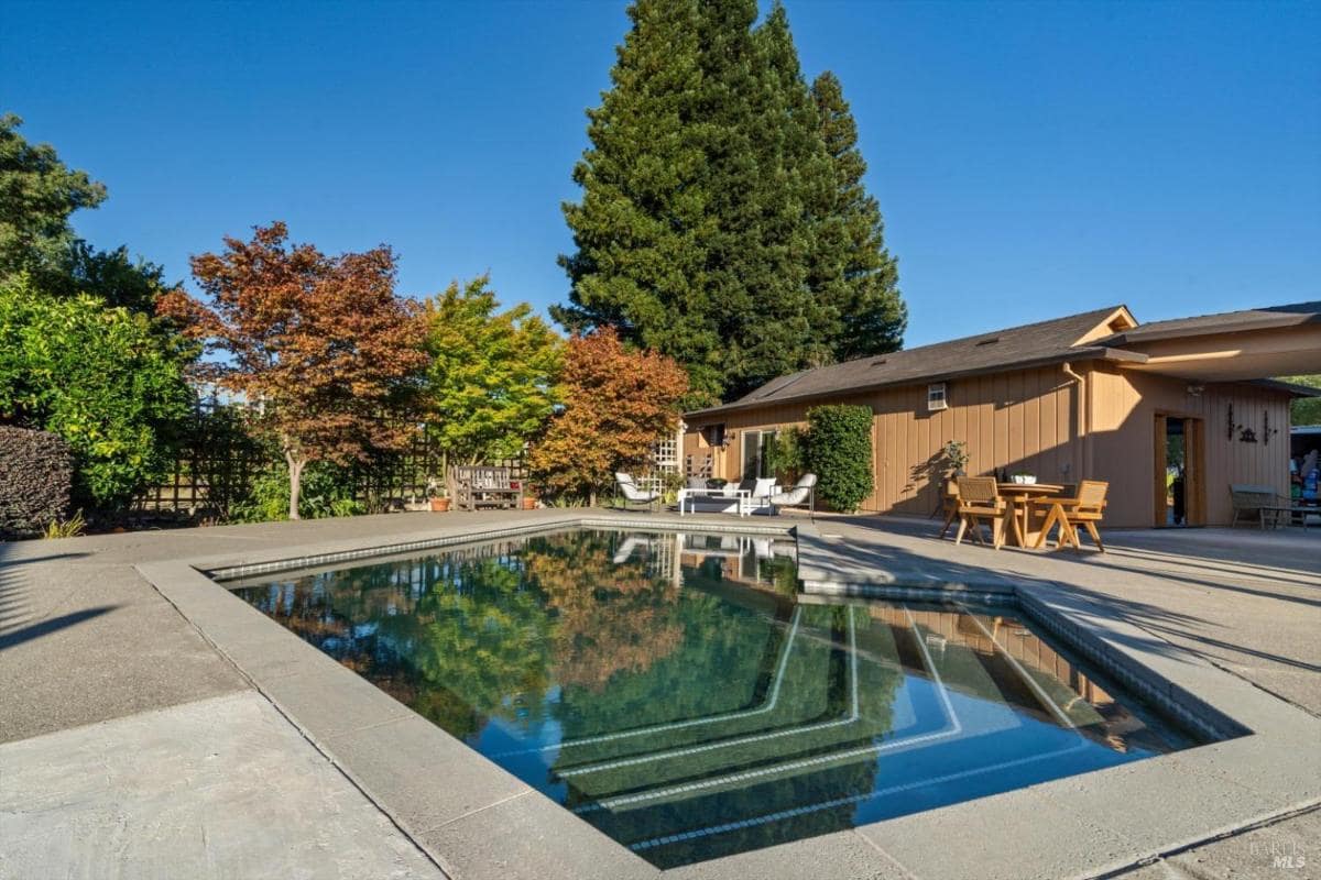 Pool area with lounge chairs, trees, and a building with outdoor seating.