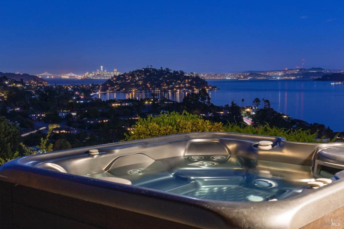 A hot tub with a scenic view of a city skyline and waterfront at night, illuminated by city lights and a bridge.