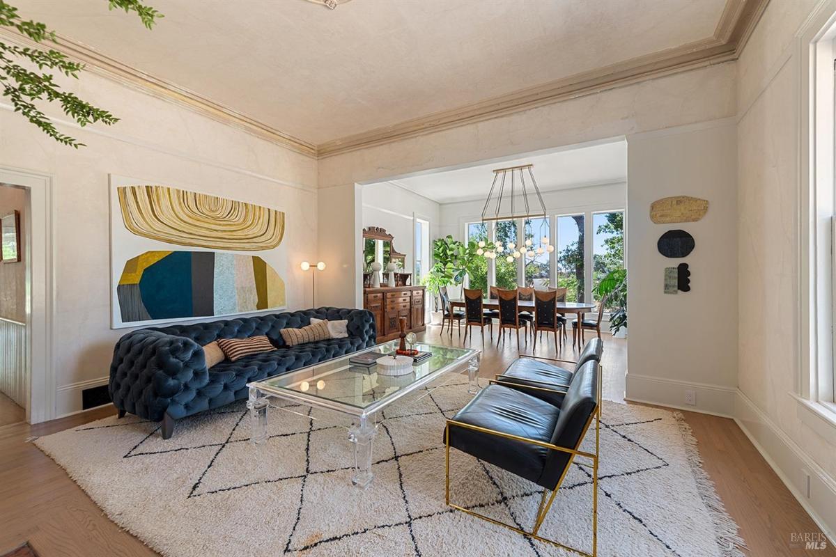 Living room with tufted blue sofa, glass coffee table, and large windows leading to dining area.