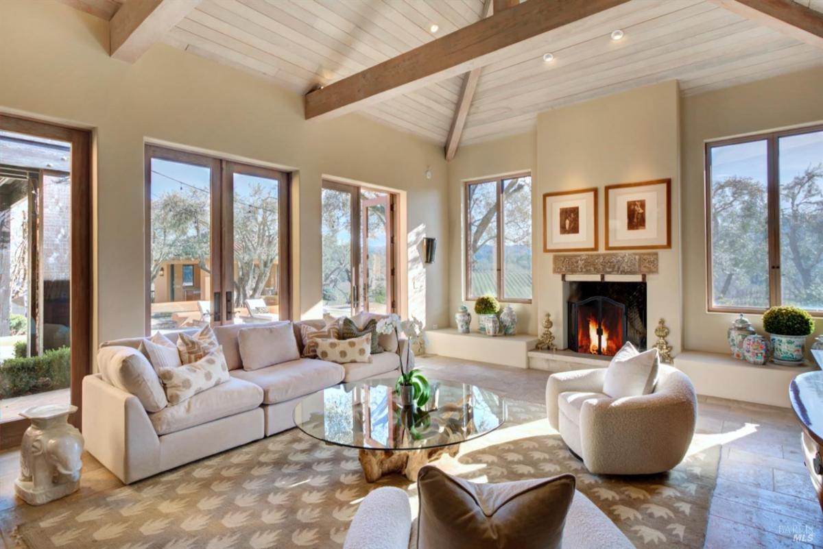 Living room with a fireplace, glass coffee table, and multiple windows opening to the outside.