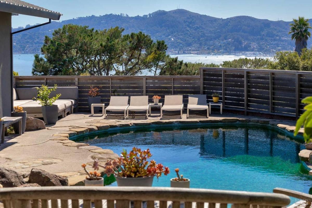A pool with lounge chairs and a view of the water and mountains in the background.