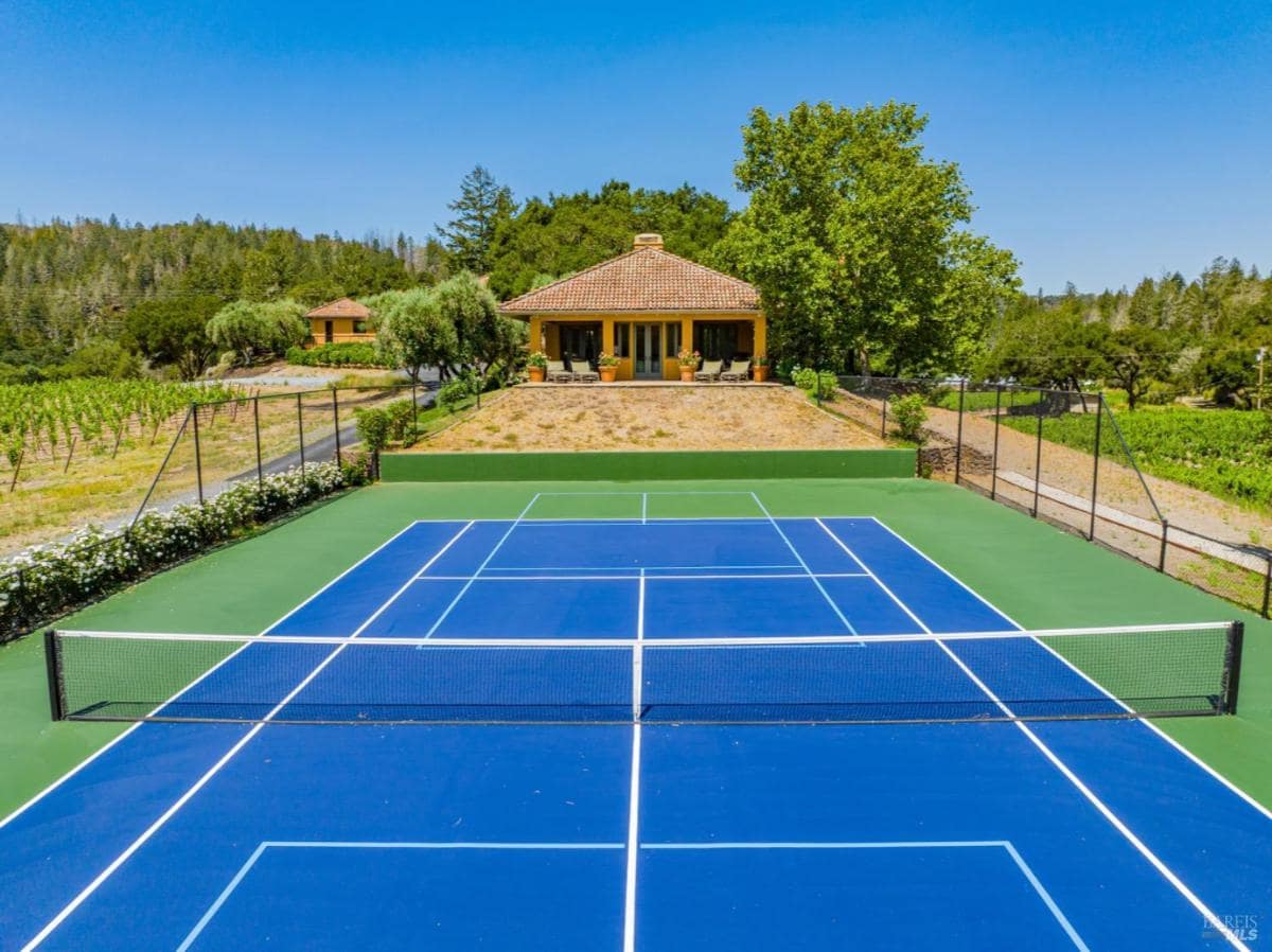Tennis court with a nearby house and vineyard views.