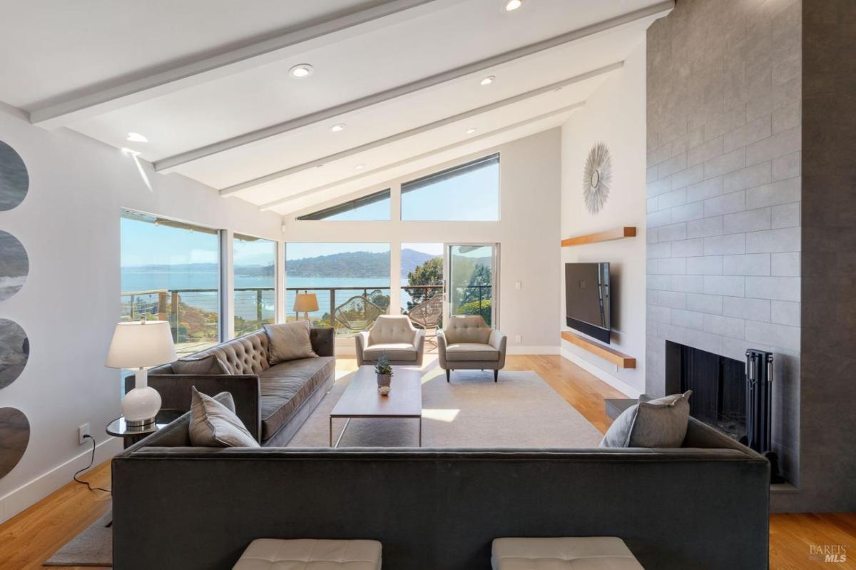 A living room with vaulted ceilings, large windows, a fireplace, and seating arranged to face the view.