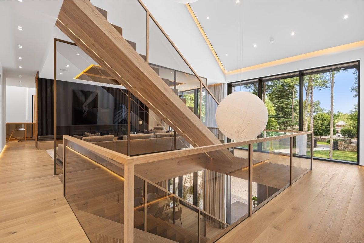 Open-concept home featuring a striking wooden staircase with glass railings. Large windows offer views of the outdoors, and the overall style is contemporary and luxurious.