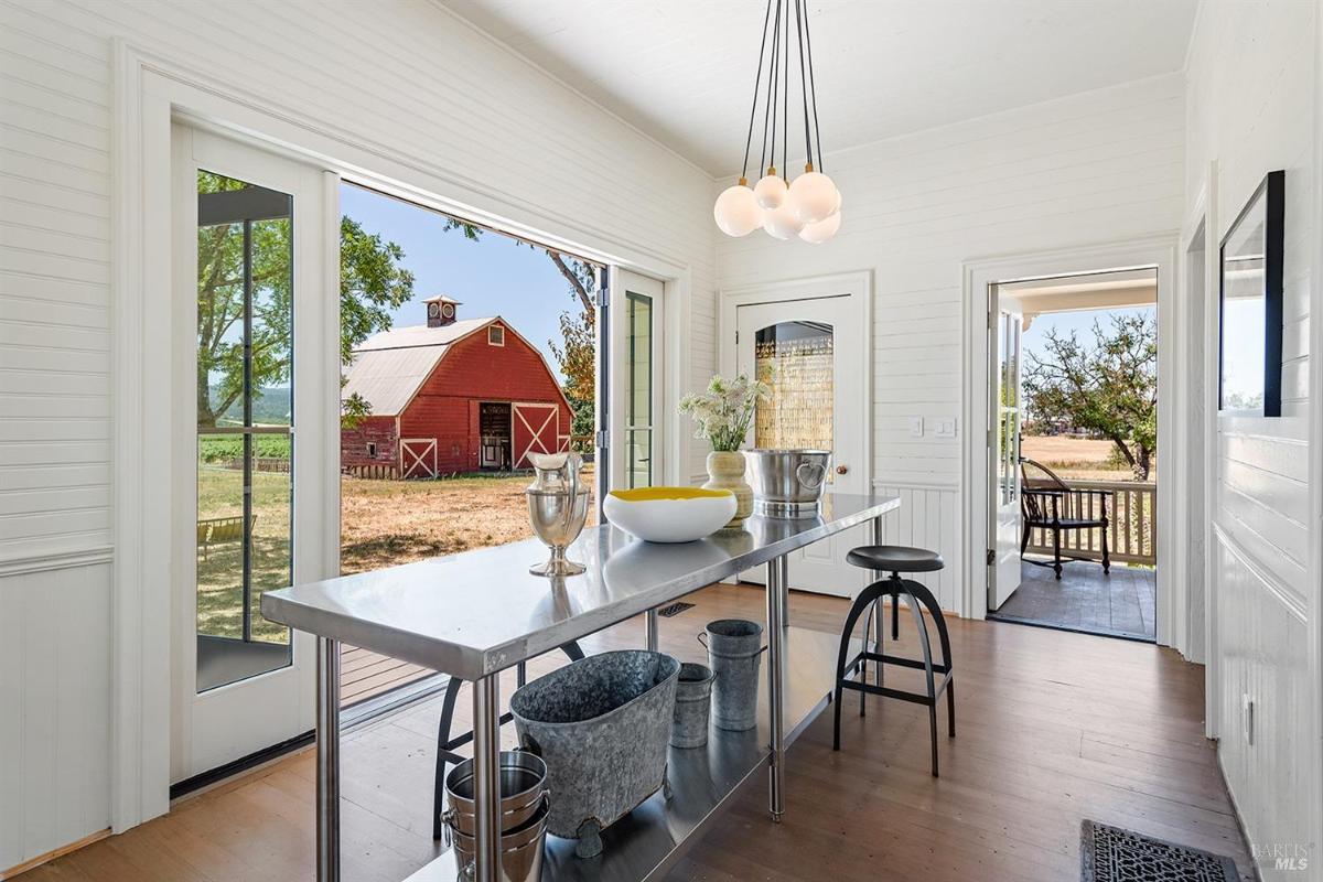 Sunroom with stainless steel table, open doors, and view of a red barn outside.