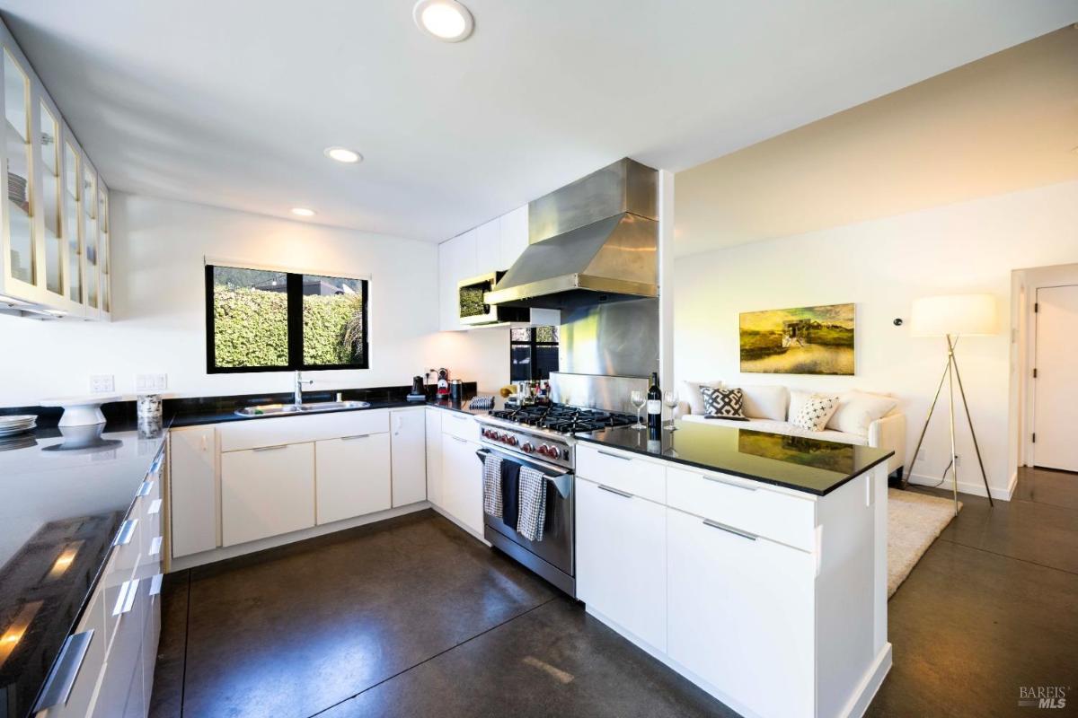 A modern kitchen featuring sleek white cabinets, a large stove with an overhead hood, and black countertops. 