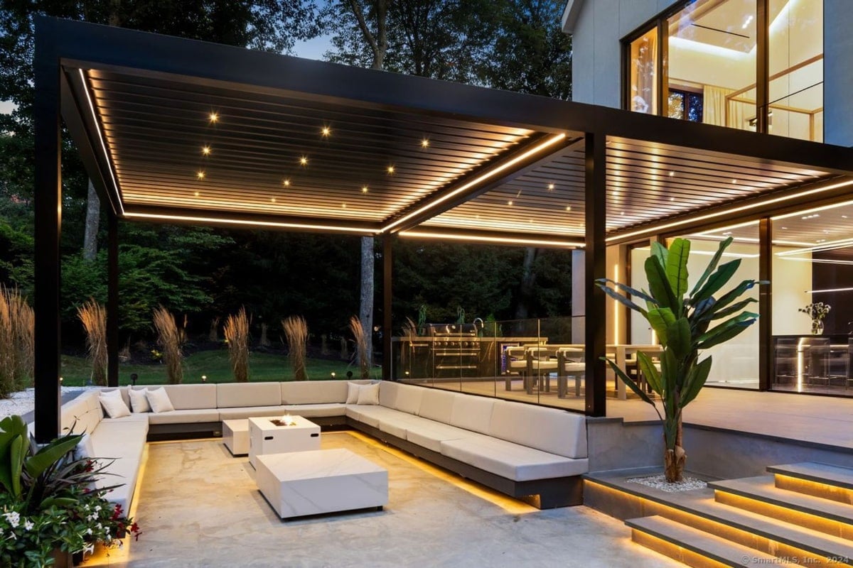 Outdoor U-shaped living space. It features a large, low-slung sectional sofa under a pergola with integrated lighting, creating a sophisticated and relaxing atmosphere.
