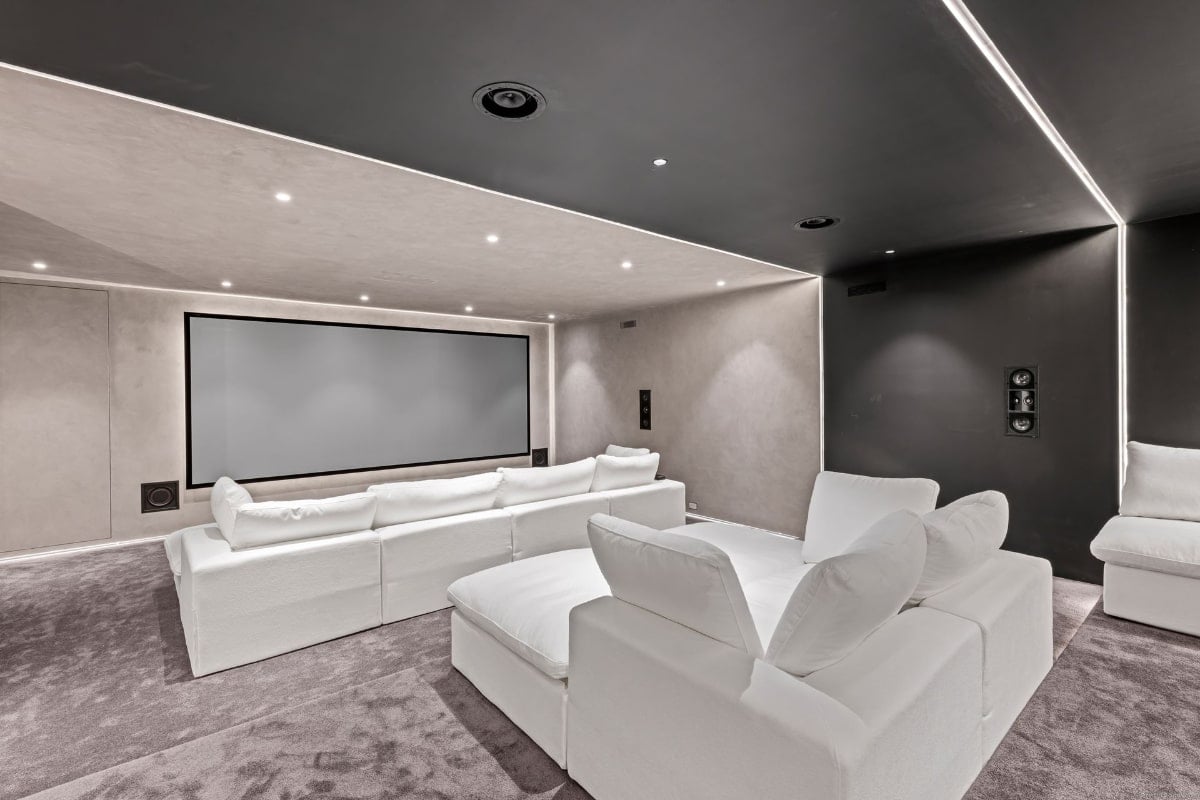 Room theater with a large projection screen and a sectional white sofa. The room has a minimalist design with a dark gray or black accent wall.