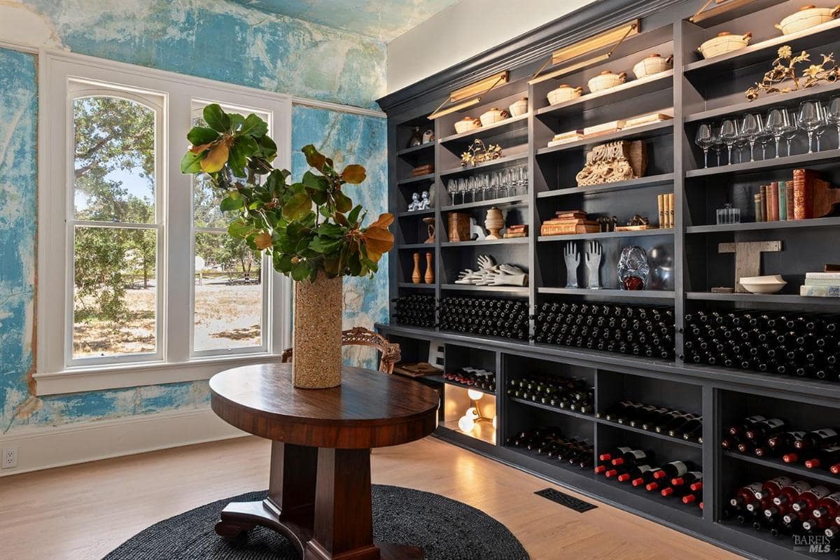 Wine room with built-in shelving, wine storage, and round wooden table under a window.