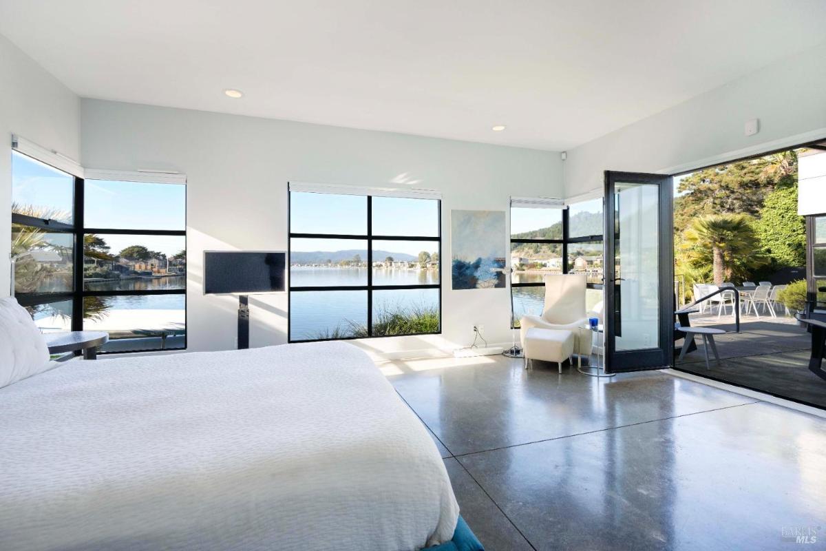 A bedroom with large windows offering a stunning view of a lake. 