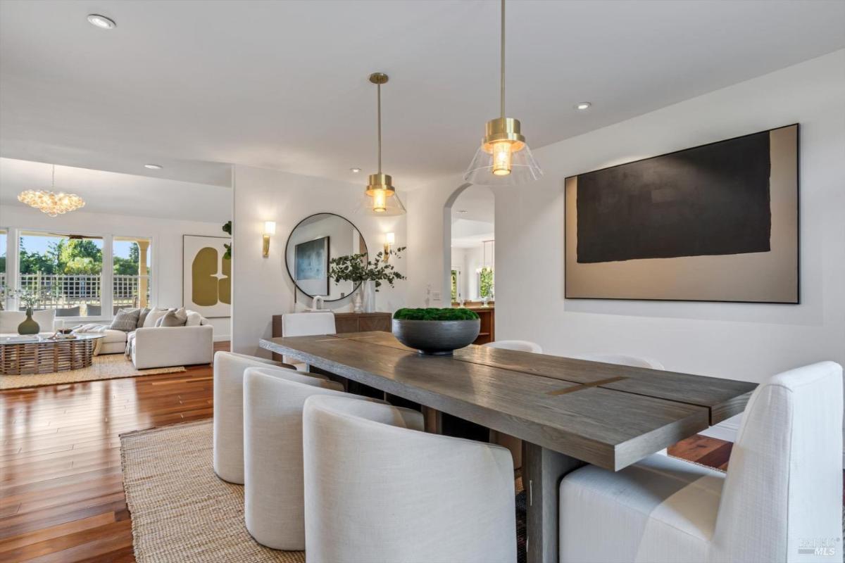 Dining area with a wooden table, white chairs, and pendant lighting, leading to a living space.