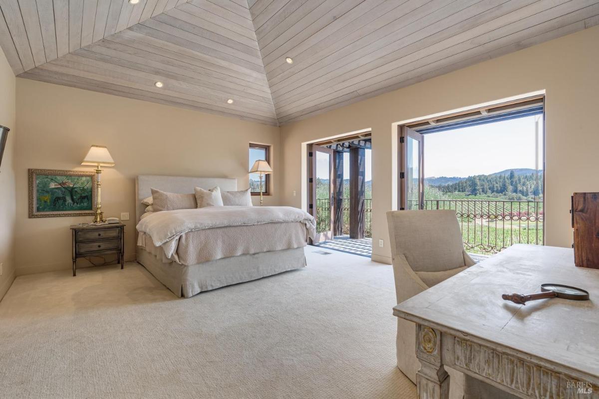 Bedroom with vaulted ceiling, bed, and balcony access overlooking the landscape.