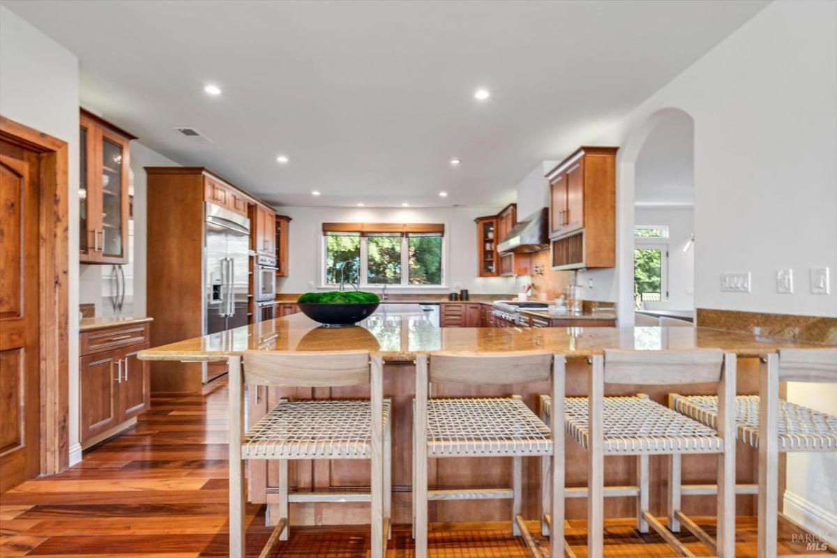 Kitchen with wood cabinetry, a large island with stools, and stainless steel appliances.