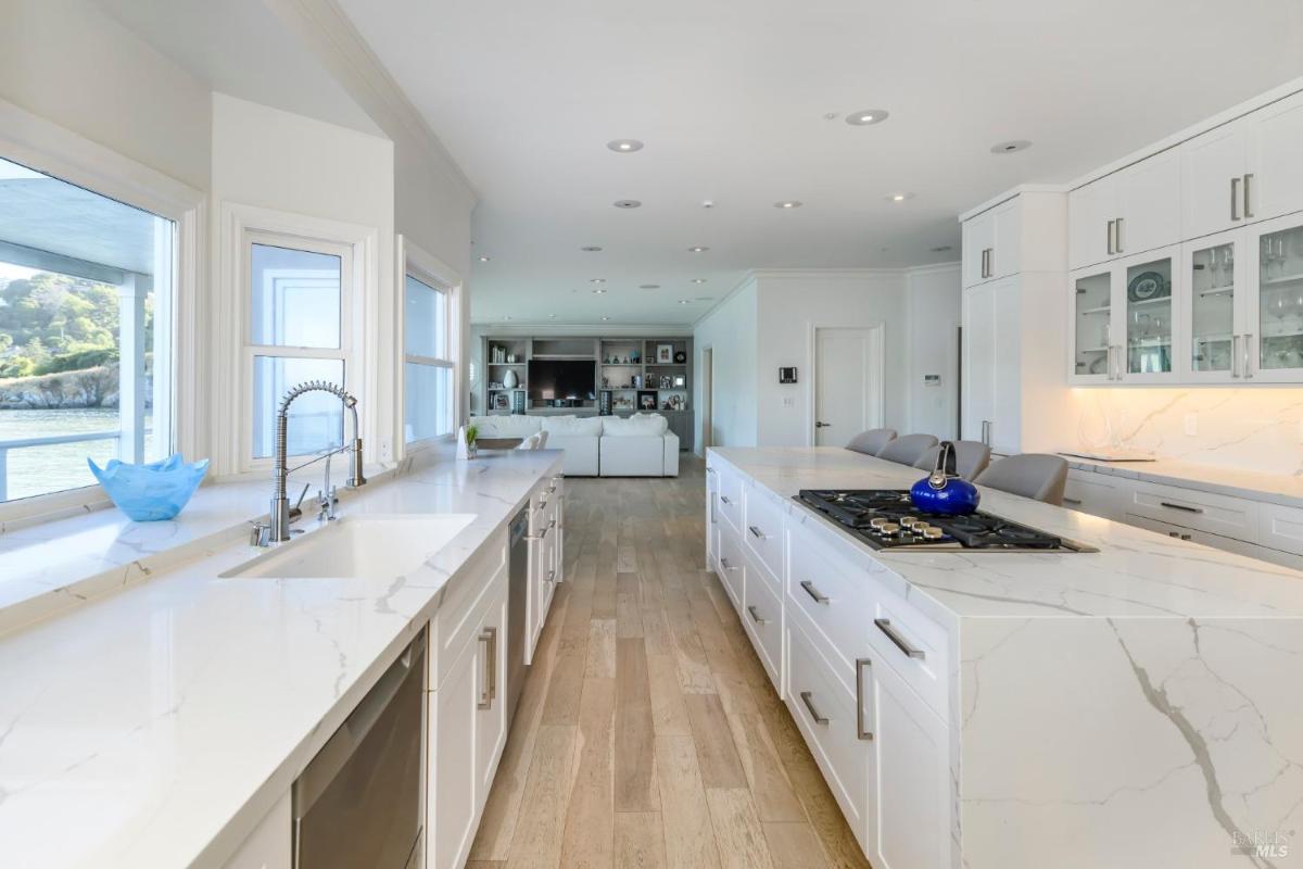 A long kitchen with white cabinetry, marble countertops, and integrated appliances.