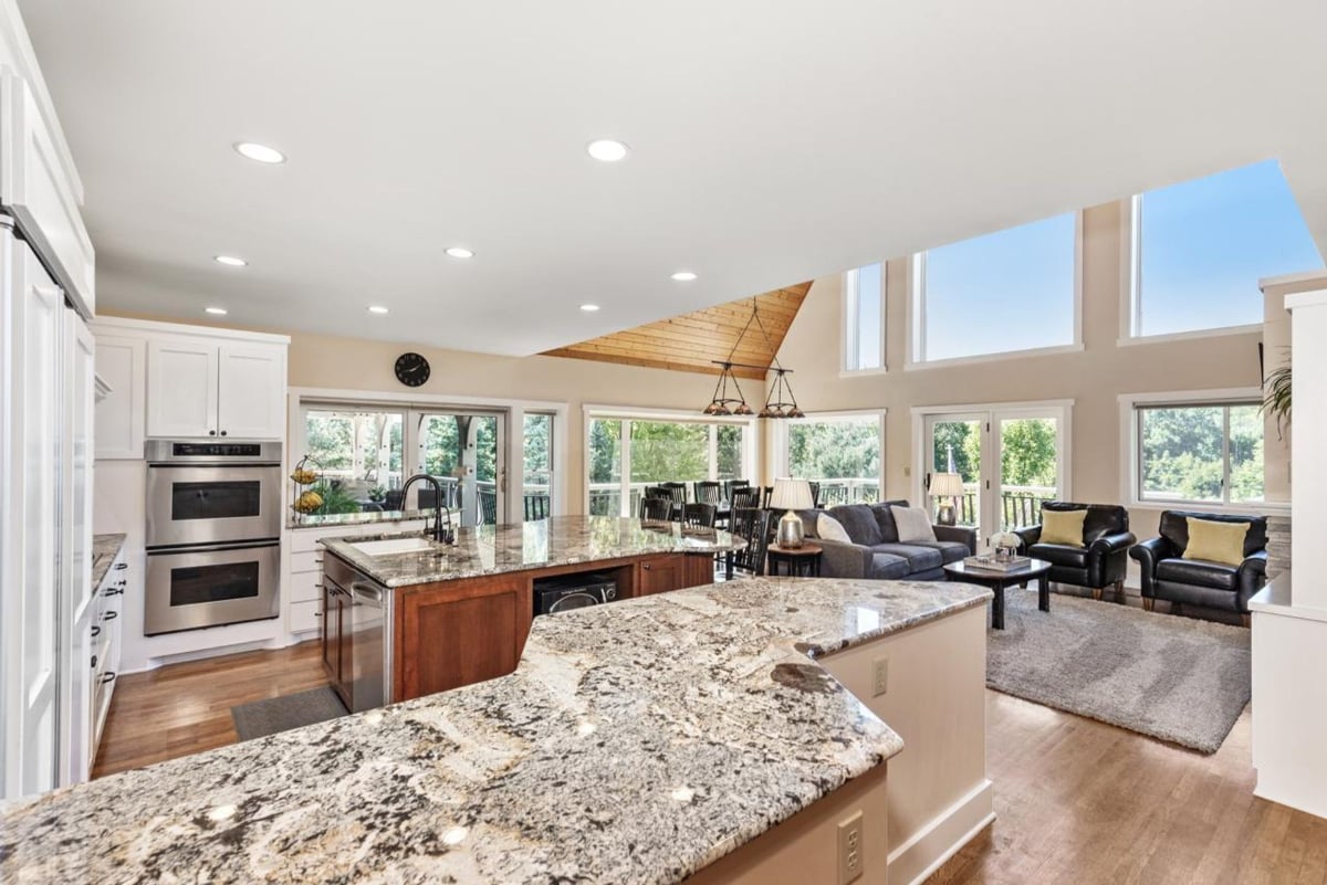 Modern kitchen with granite countertops, stainless steel appliances, and an open floor plan that flows into a living area with large windows and high ceilings.