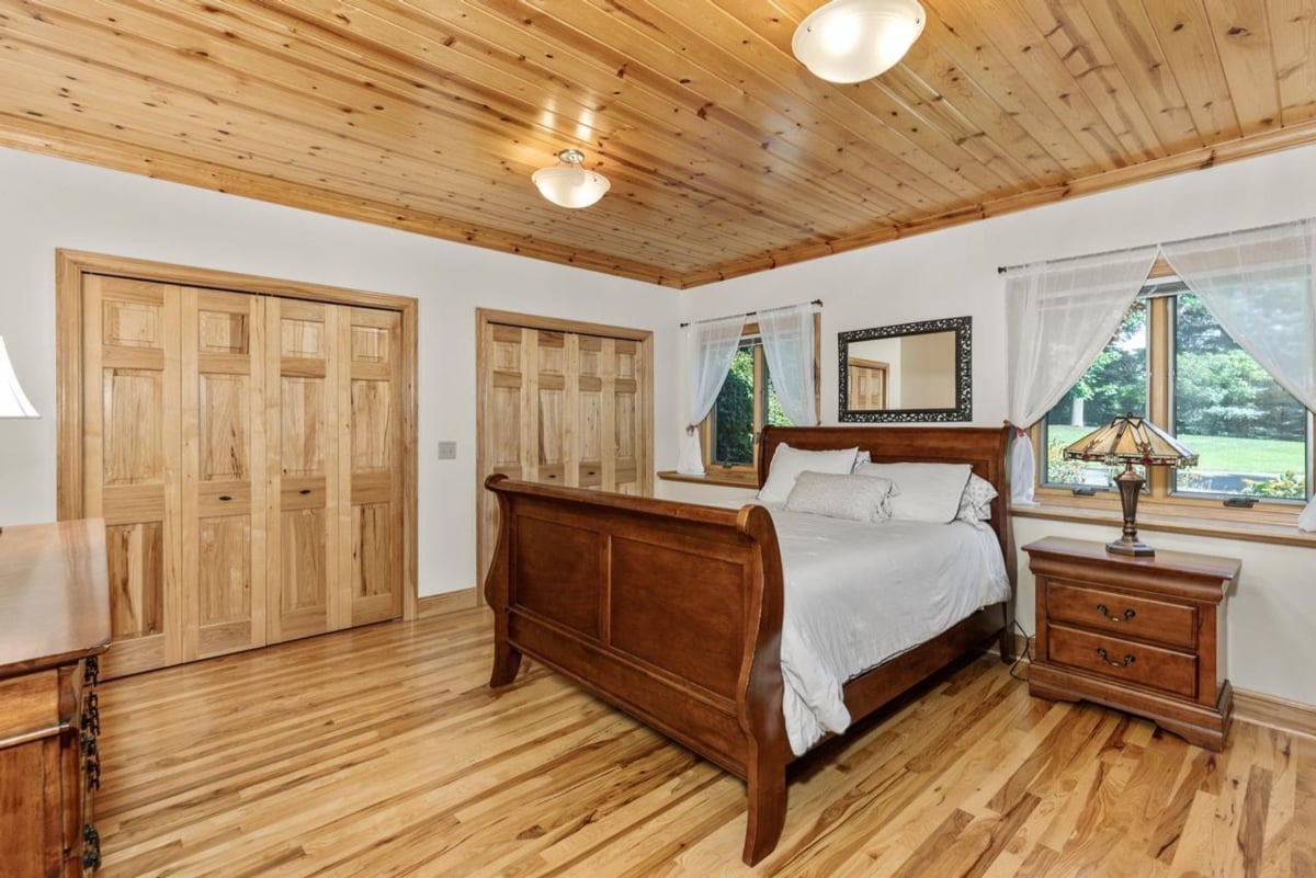 Bedroom features hardwood floors, a sleigh bed, wood-paneled ceilings, and large windows that let in plenty of natural light. 