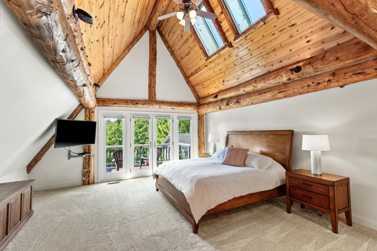 Master bedroom features a vaulted ceiling with exposed wooden beams, a ceiling fan, and large windows.