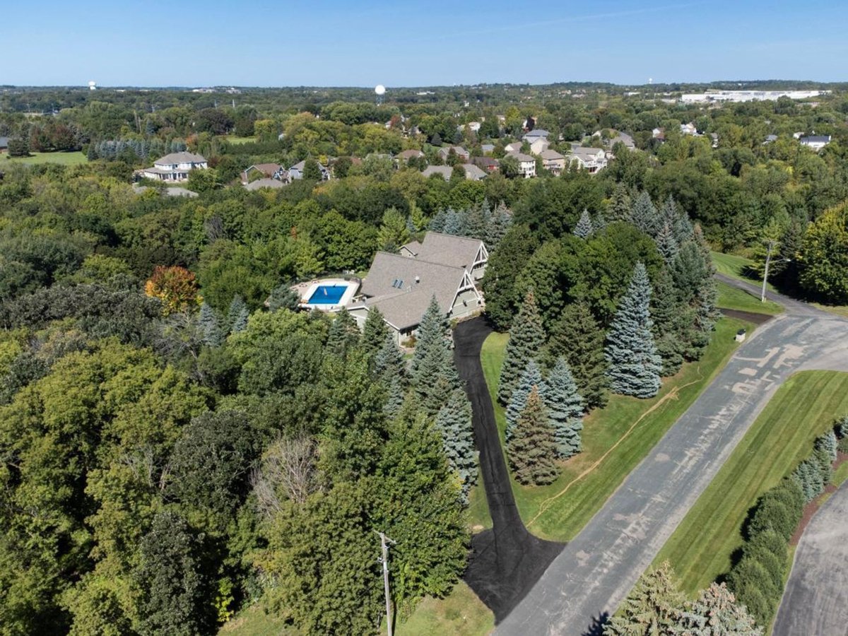 An aerial view reveals a house, private pool, and long driveway nestled within a lush, tree-filled landscape.