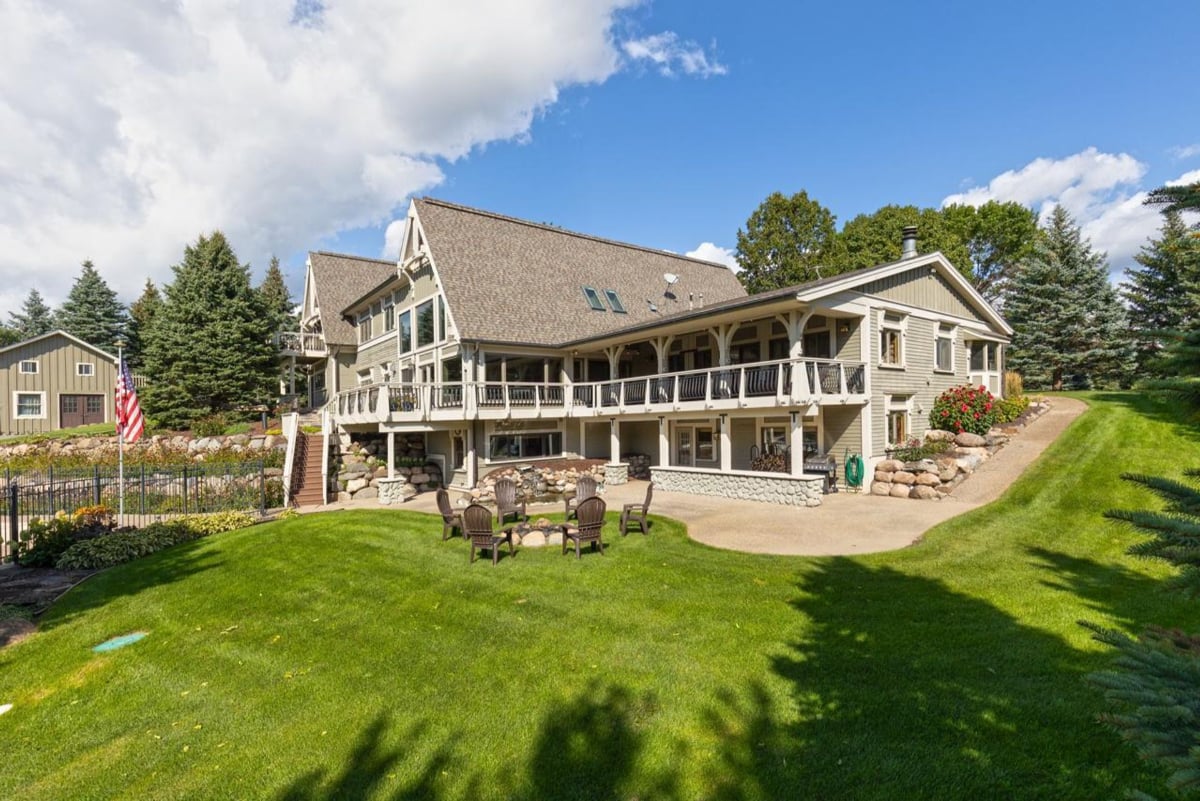 A large home with a wrap-around porch sits on a grassy lawn.