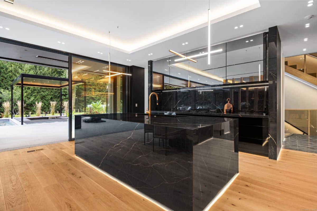 Kitchen with dark marble countertops and cabinetry. Large windows offer a view of an outdoor area, and the flooring appears to be light-colored wood.