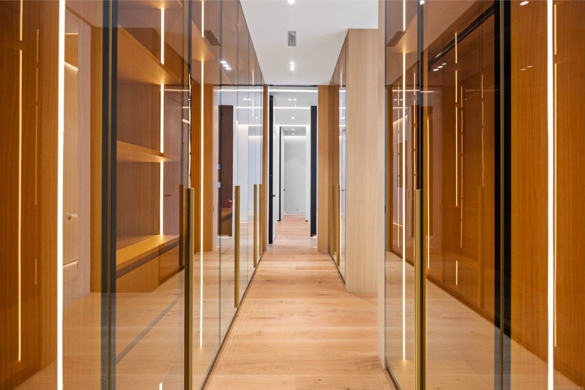 A narrow hallway with a modern design. The walls are lined with wood-paneled doors and glass partitions, creating a sleek and contemporary atmosphere. The floor is light-colored, and the overall impression is one of clean lines and minimalist aesthetics.