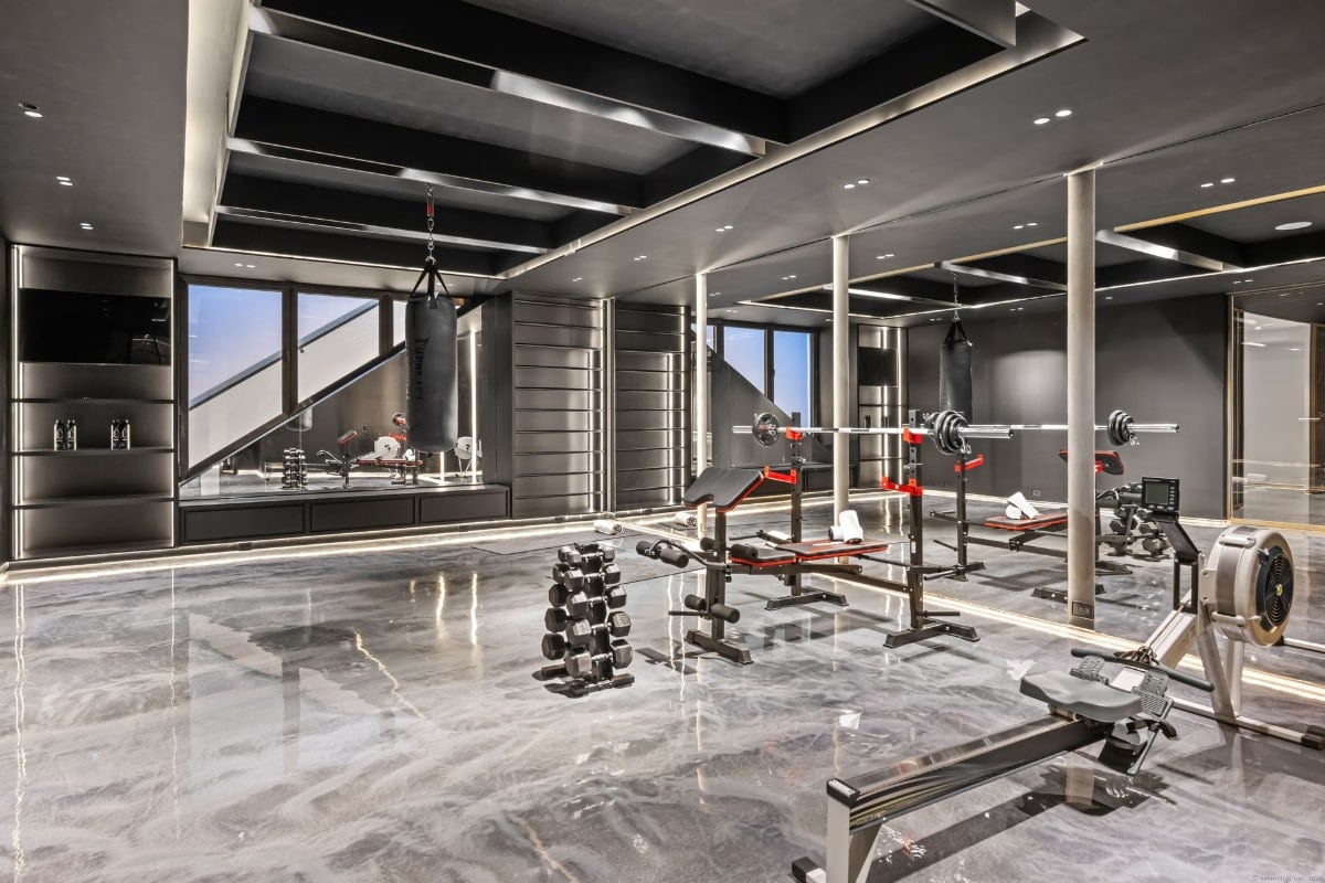 Well-equipped home gym. The space is predominantly dark-colored, with various weight training equipment, a rowing machine, and a punching bag.