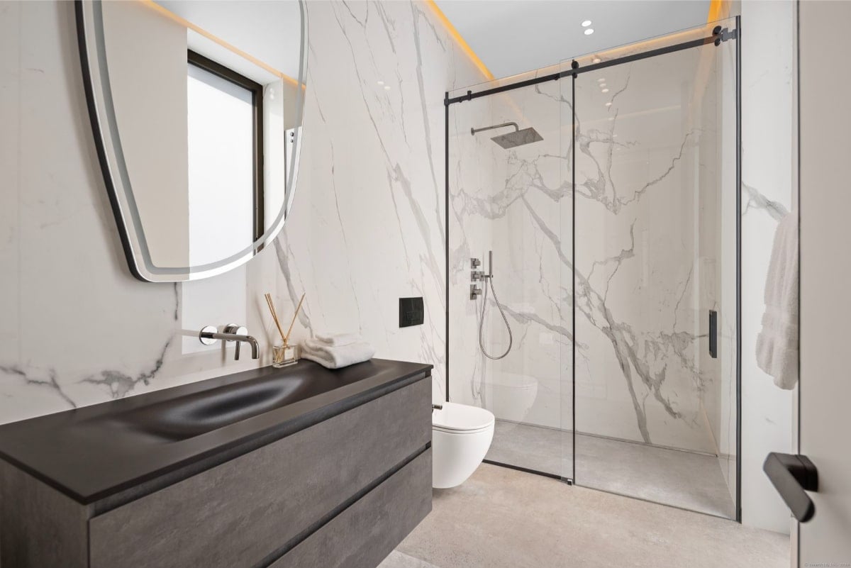 Bathroom with marble walls and a frameless glass shower enclosure. The sink is a dark gray or black integrated countertop style.